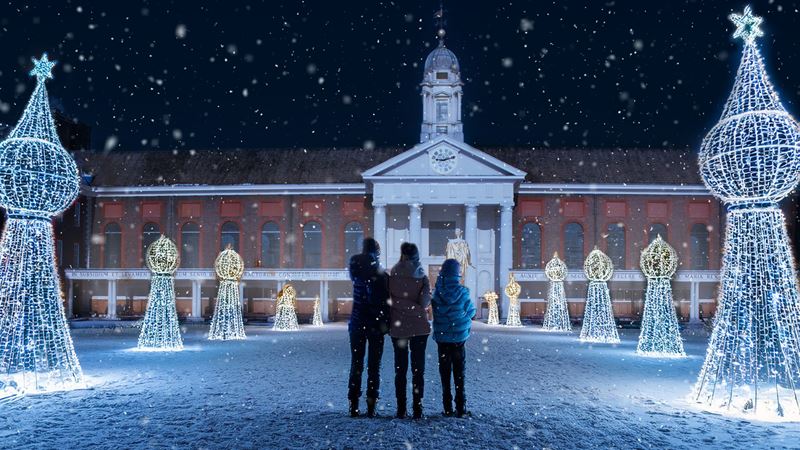 Step into the winter wonderland in the heart of Chelsea at Christmas in Chelsea. Credit: Golden Tours. Image courtesy of Golden Tours. an exterior photo of an old red brick building, with three people stood amongst light installations and snow