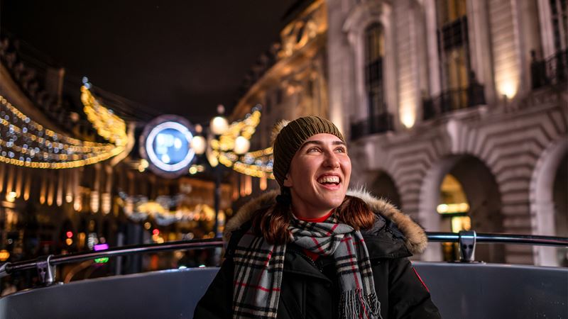 Take in the festive lights from the London by Night Christmas Lights Tour. Credit: Michael Barrow. Image courtesy of London & Partners. A young lady wrapped up warm enjoying the festive lights from a bus tour.