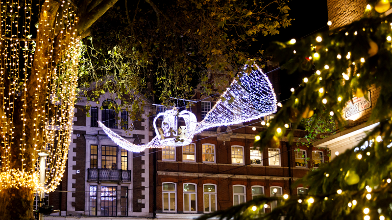 See the twinkling Christmas decorations light up Chelsea's streets during winter. Credit: Karolina Krasuska. Image courtesy of Chelsea. Christmas decorations hanging above the King's Road at night, including a bright LED crown and twinkling gold string lights with the side of a Christmas tree in the foreground