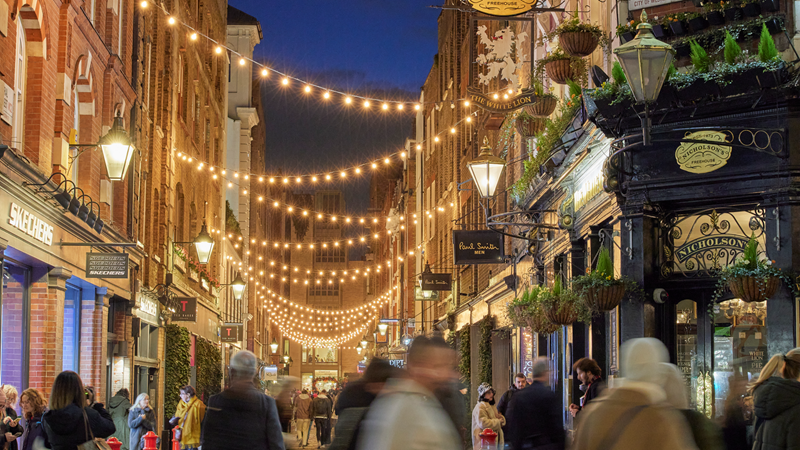 Tick off Christmas wishlists from some of the best London shops dotted around Seven Dials and Covent Garden. Credit: Covent Garden. Image courtesy of Covent Garden. Warm strings of Christmas lights hand above a street in Seven Dials as people pass by the shop windows in the evening
