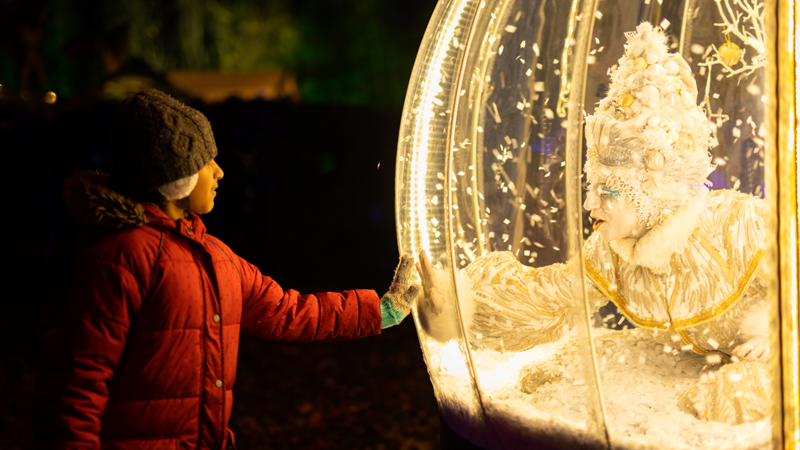 Marvel at the wonderful installations dotted around Sparkle in the Park in south London. Credit: Royal Borough of Greenwich. Image courtesy of Royal Borough of Greenwich. A young child dressed in a red coat and beanie hat touches a giant light up globe with an actress dressed up in a winter-themed outfit looking back at them