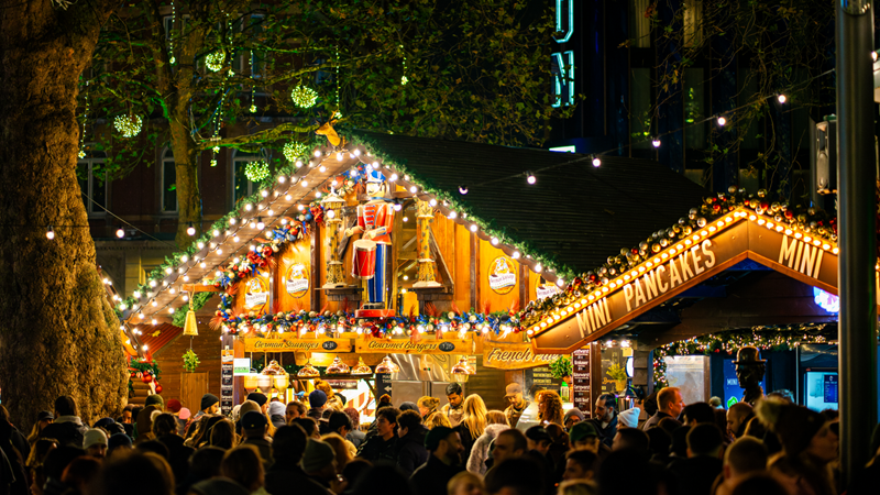 Spot the twinkling lights at Leicester Square Christmas market and the surrounding area. Credit: Michael Aiden. Image courtesy of Leicester Square. Warm twinling lights illuminate a stall at the Leicester Square Christmas market with a toy soldier on the top and crowds of people walking around in front