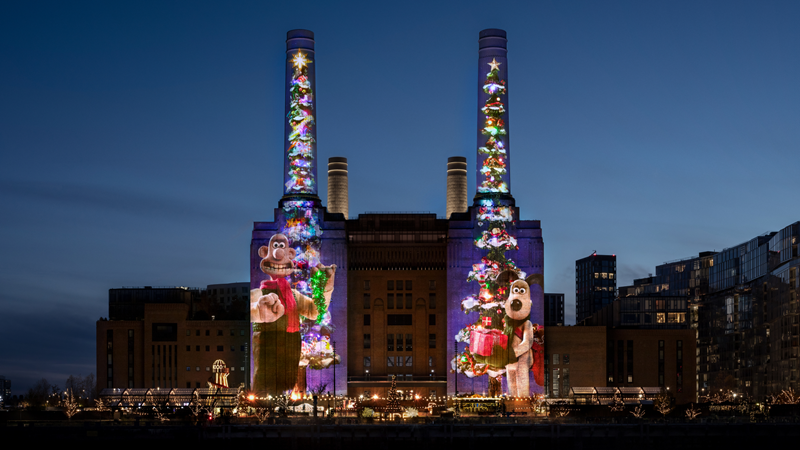 Spot the Battersea Power Station Christmas tree this year featuring the beloved Wallace and Gromit. Credit: Battersea Power Station. Image courtesy of Battersea Power Station. A photo of Battersea Power Station at night with a projection of Wallace on the left chimney and Gromit on the right chimney of the iconic building, wearing red scarves and holding a pile of presents that each form a Christmas tree shape