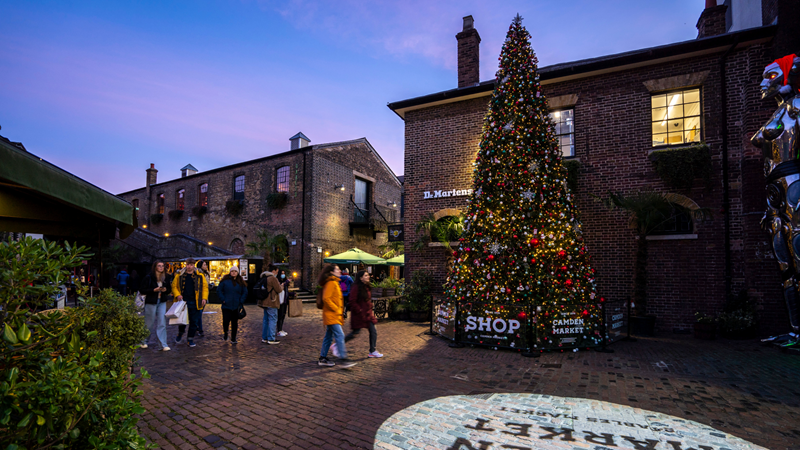 Try to spot all five Christmas trees dotted around Camden Market this Christmas! Credit: Camden Market. Image courtesy of Camden Market. A large Christmas tree covered in twinkling lights and baubles stands outside of the Cyberdog shop in Camden Market, next to two giant silver robots wearing santa hats stood outside the shop entrance