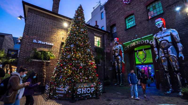 Try to spot all five Christmas trees dotted around Camden Market this Christmas! Credit: Camden Market. Image courtesy of Camden Market. A large Christmas tree covered in twinkling lights and baubles stands outside of the Cyberdog shop in Camden Market, next to two giant silver robots wearing santa hats stood outside the shop entrance