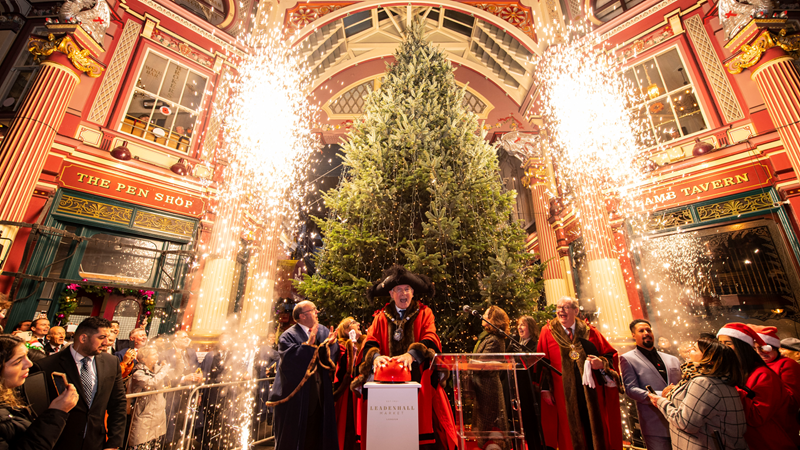 Head to the City of London's Victorian market, where you'll find the famous Christmas tree switched on by the Lord Mayor of London each year. Credit: Lucy Young. Image courtesy of Leadenhall Market. The Lord Mayor of London pushing a large red button as lights switch on the large Christmas tree inside Leadenhall Market, surrounded by crowds of people