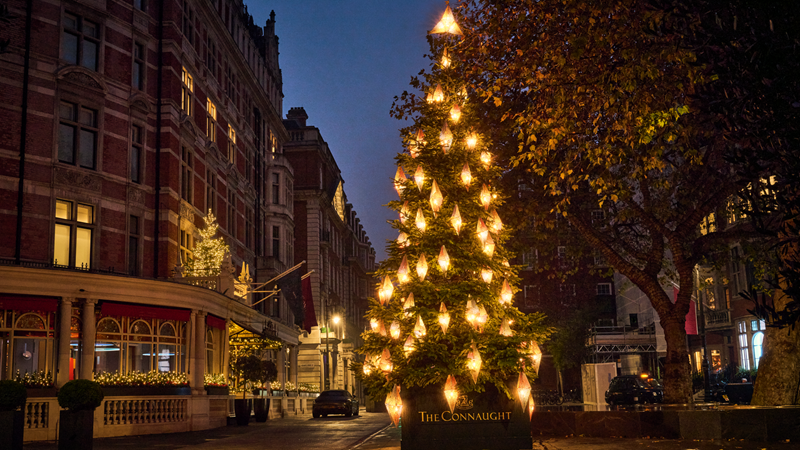 See The Connaught Christmas tree light up Mayfair with its 90 glowing lanterns and star. Credit: The Connaught. Image courtesy of The Connaught. A photo of the square in Mayfair with a large fir tree covered with gold glowing lanterns with a star at the top with The Connaught hotel logo at the bottom