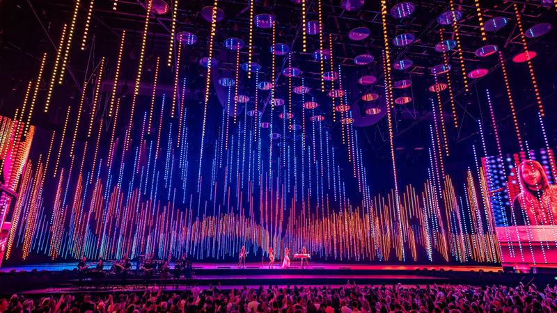 ABBA Voyage performance of Dancing Queen at London's ABBA Arena. Credit: Johan Persson. Image courtesy of ABBA Voyage. ABBA Arena stage lit up in pink, orange and purple lights during a live performance of ABBA Voyage in London.