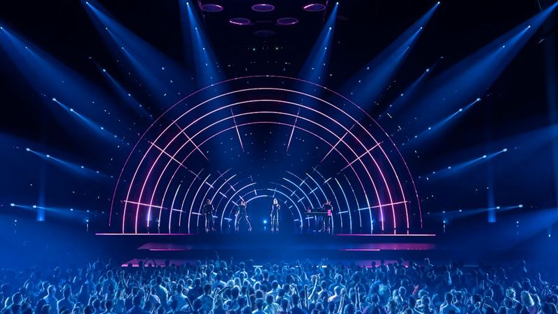 ABBA Voyage performance of Gimme, Gimme, Gimme at London's ABBA Arena. Image courtesy of Johan Persson / ABBA Voyage. ABBA Arena stage lit up in pink and blue lights during a live performance of ABBA Voyage in London.