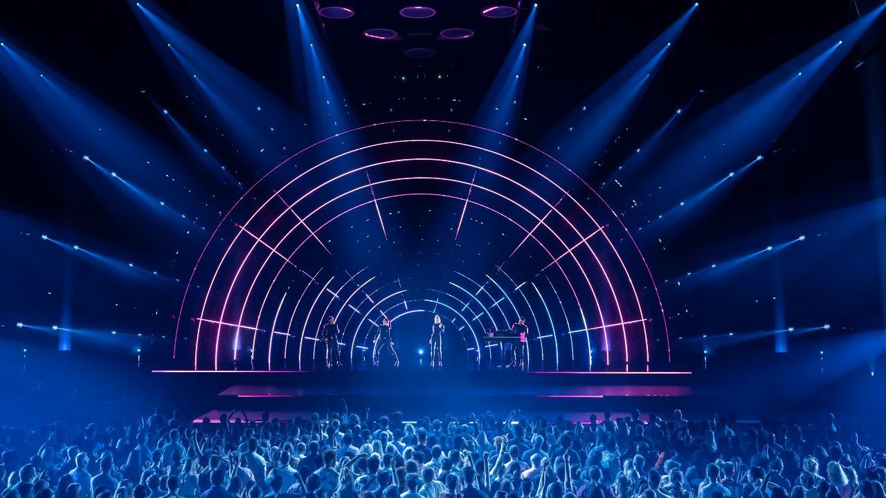 ABBA Voyage performance of Gimme, Gimme, Gimme at London's ABBA Arena. Image courtesy of Johan Persson / ABBA Voyage. ABBA Arena stage lit up in pink and blue lights during a live performance of ABBA Voyage in London.