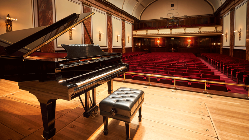 Find live music events spanning a multitude of genres at Wigmore Hall. Credit: Kaupo Kikkas. Image courtesy of Wigmore Hall. A grand piano and stool on the stage at Wigmore Hall with red velvet seats in the background