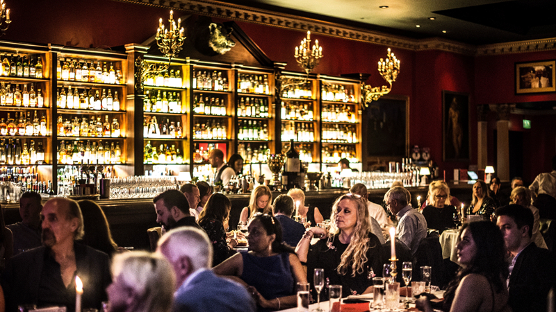 Crowds sit at round tables with a backdrop of warm lighting at Boisdale Canary Wharf