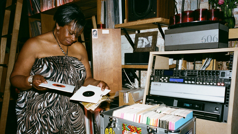 Watch artists flick through their favourite records at Jumbi. Credit: India Morgan. Image courtesy of Jumbi. Female DJ taking disc out of record sleeve with records and music hardware in background