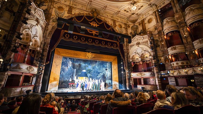 The spectacular setting of the London Coliseum. Credit: Lloyd Winters. Image courtesy of London Coliseum. A performance with spectators inside the grand-looking London Coliseum theatre.