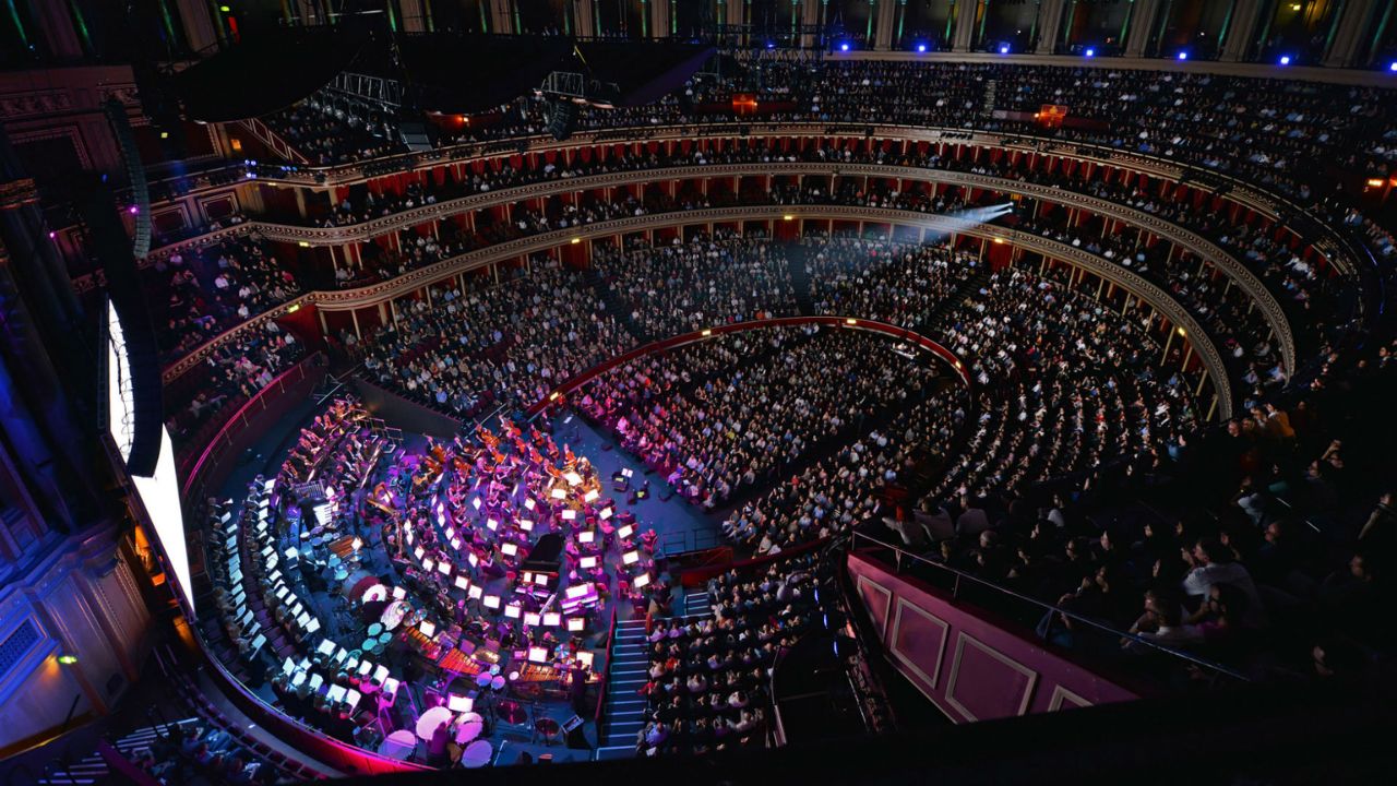 The ominously lit Royal Albert Hall auditorium filled with people watching a bright screen.