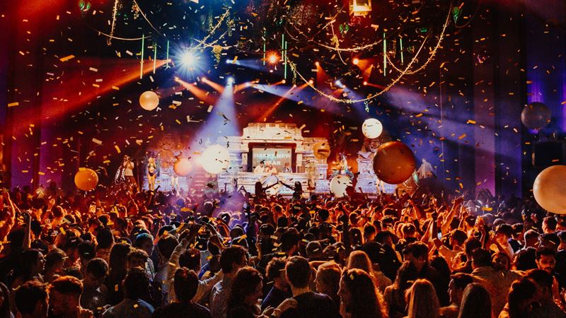 Dance all night at Troxy's legendary New Year's Eve party. Credit: Ben McQuaide. Image courtesy of Cirque Du Soul. New Year's Eve party at London club Troxy with crowds dancing, and confetti and balloons in the air.