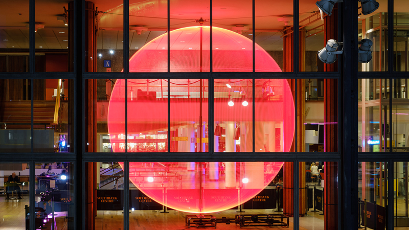 Marvel at eye-catching light installations dotted around South Bank for the Southbank Centre's Winter Light. Credit: Owen Billcliffe. Image courtesy of Southbank Centre. A giant red glowing light projected onto windows at the Southbank Centre at night, with the entrance to the building below
