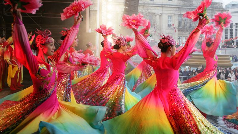 Experience the colourful Chinese New Year celebrations in London. Credit: LCCA. Image courtesy of LCCA. A group of brightly dressed dancers perform on a stage in front of crowds in Trafalgar Square during Chinese New Year in London