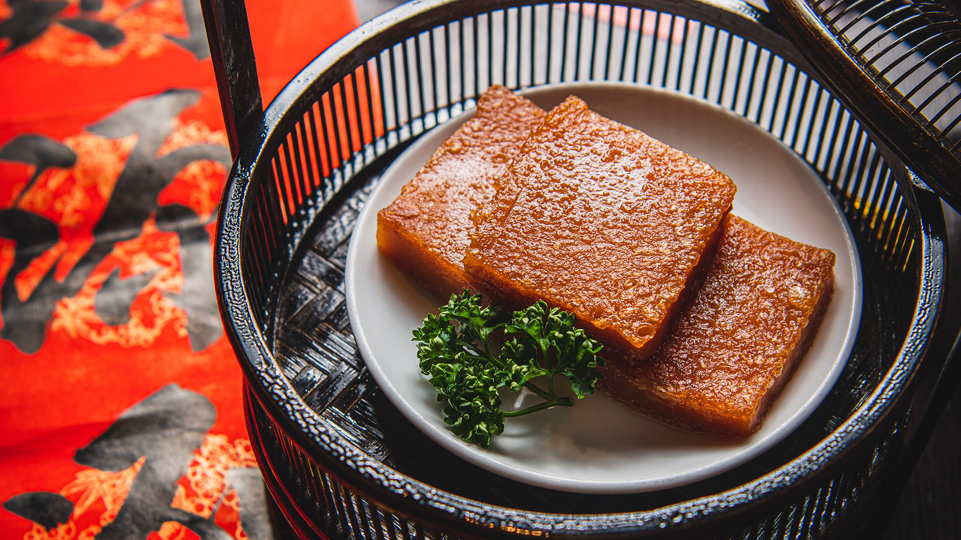 Nian Gao served in a basket. Image courtesy of Street & Co. Credit: Nic Crilly-Hargrave. Nian Gao served on a white plate with some garnish next to it in a black basked standing on a black table with Chinese decorations.