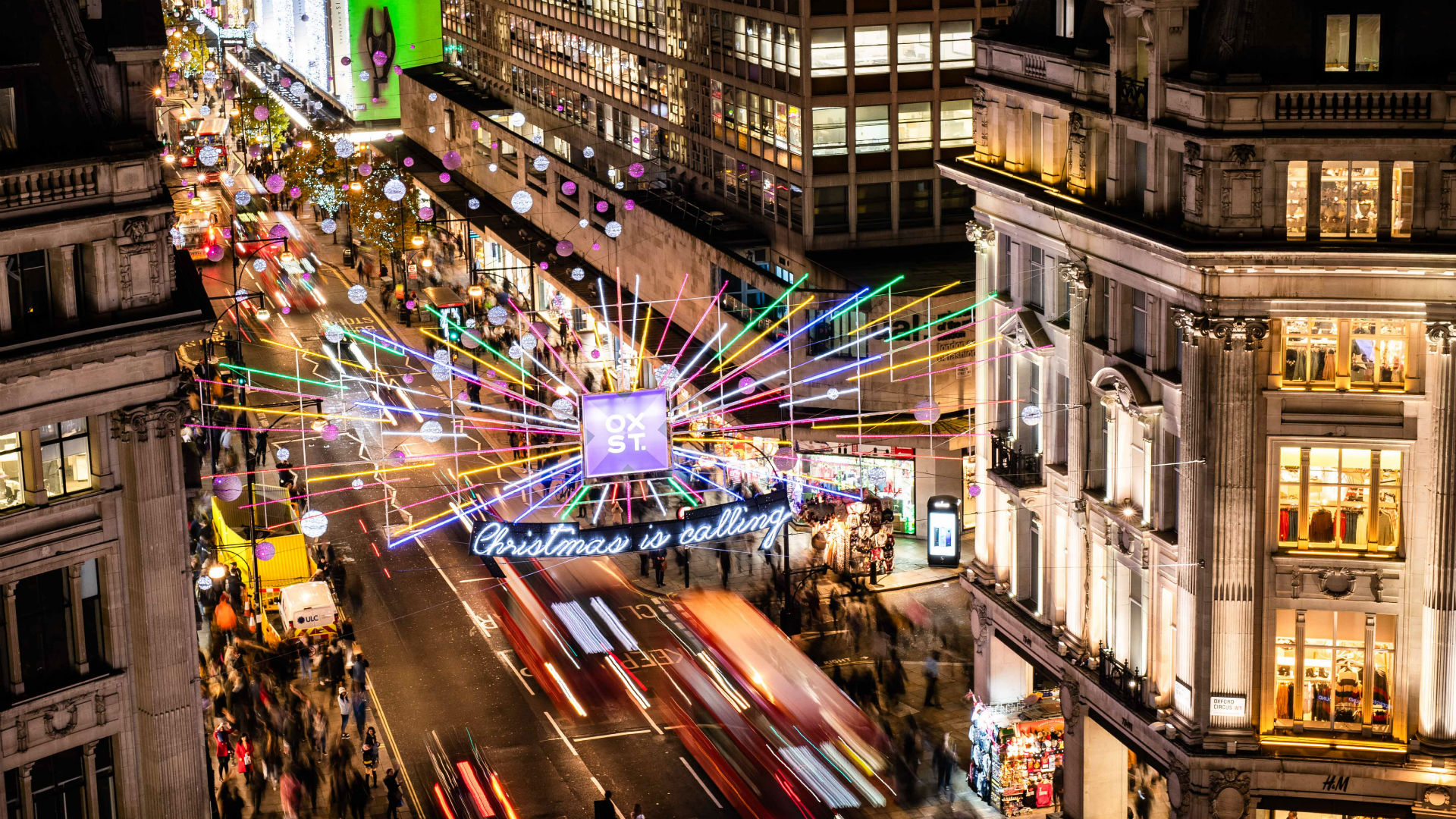 Shops on Oxford Street have varying closing times. ©John Nguyen/PA Wire. Image courtesy of NWEC. Rainbow-coloured Christmas lights sparkle above the buzzing streets of Oxford Street at night.