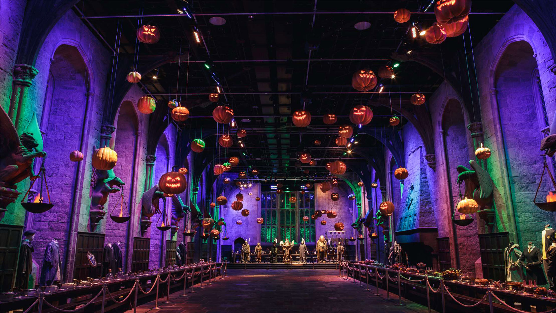 Pumpkins decorate the Great Hall at the Warner Bros. Studio Tour London for Halloween. Image courtesy of Warner Bros. Studio Tour London - The Making of Harry Potter. The Great Hall Harry Potter film set is filled with floating pumpkins and purple light for Halloween.