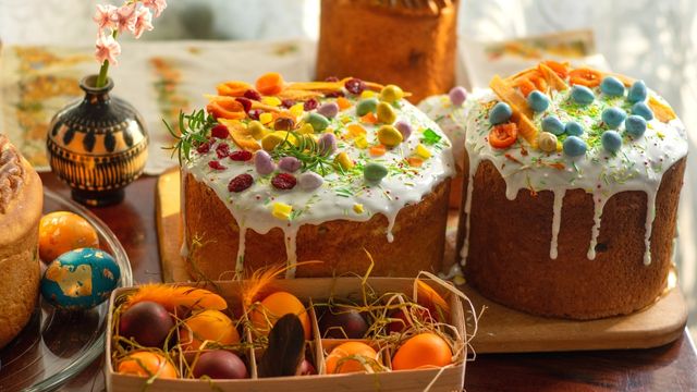 Indulge in sweet treats this Easter. © visitlondon.com/Elena Mozhvilo A tray of orange eggs in straw and two large easter cakes with colourful eggs and white dripping icing.