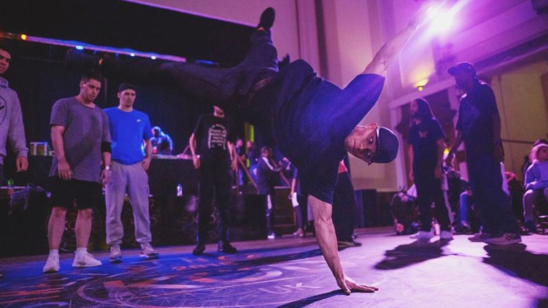 Catch showstopping performances and get involved in movement workshops at Strictly Wandsworth. Credit: Gully Ldn. Image courtesy of Wandsworth. A photo of a man balancing on one hand with his legs and other arm in the air during a breakdance as people watch him and the lights shine pink
