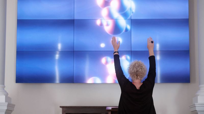 See creative works and art exhibitions at venues across Wandsworth during its annual art fringe festival. Credit: Cave and Sky. Image courtesy of Wandsworth Arts Fringe. A photo of a woman from behind holding her arms up in front of a giant interactive screen with blue and pink coloured artwork