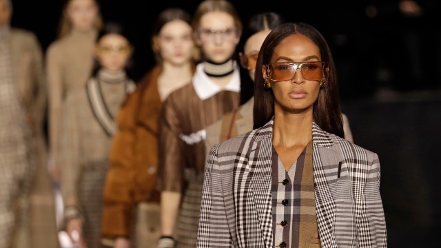 Burberry designs on the catwalk at London Fashion Week. Image courtesy of British Fashion Council/Getty. Ladies walking in line presenting clothes during a fashion show.