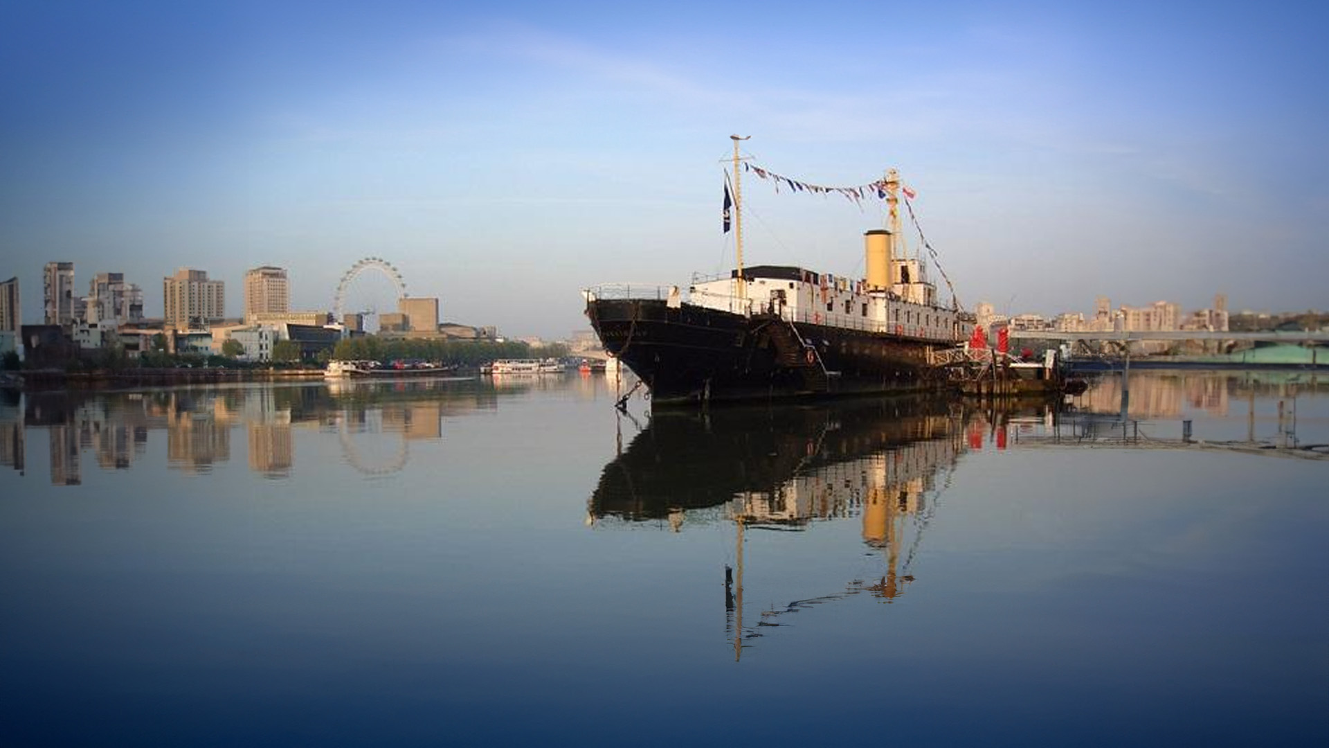 Hop aboard the iconic HMS President (1918) Image courtesy of HMS President (1918) An old boat sits on top of a river with a blue sky and city backdrop