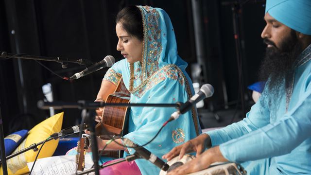Vaisakhi in Trafalgar Square. Credit: Greater London Authority. Image courtesy of the Greater London Authority. Two people playing instuments on stage, dressed in light blue clothing.