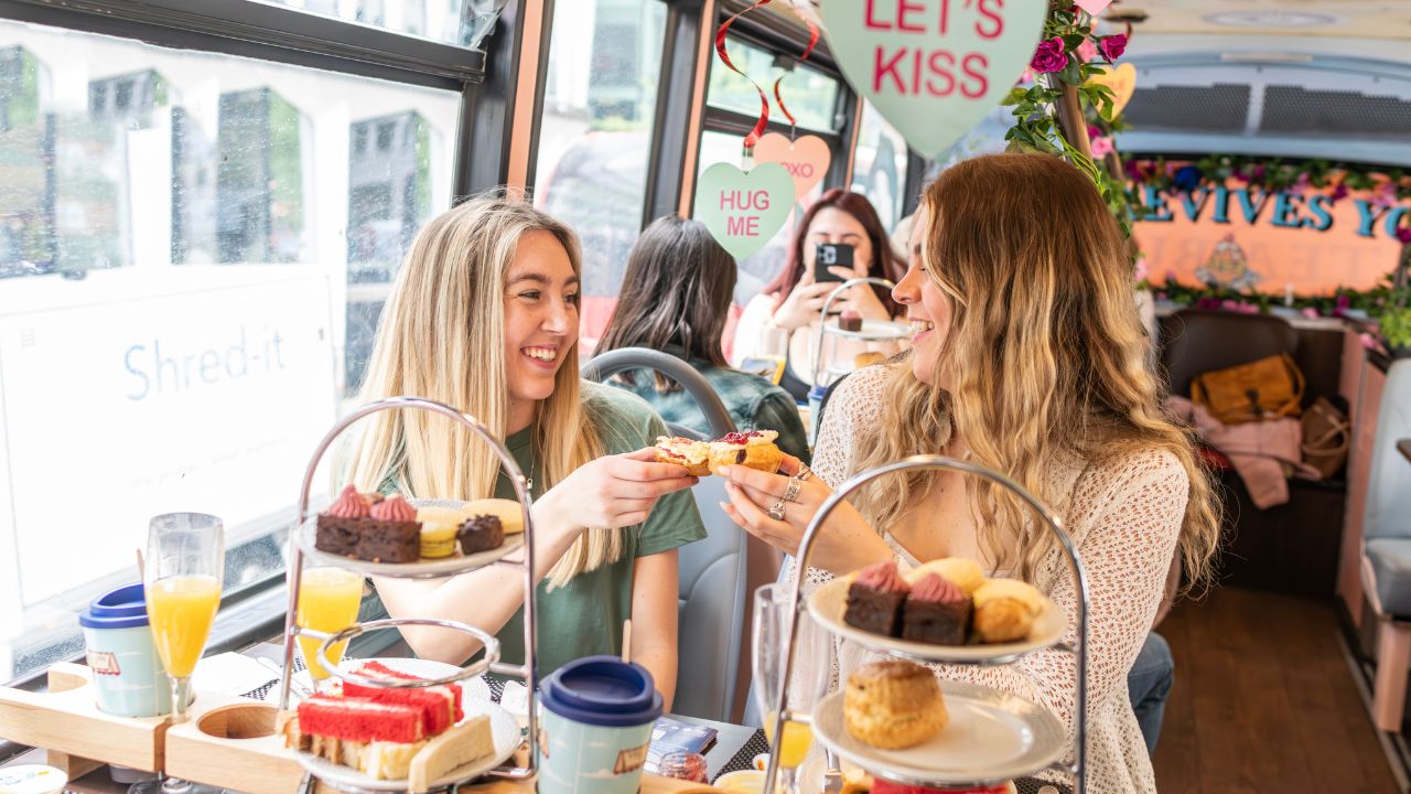 Two people cheers drinks aboard a valentines themed afternoon tea bus tour