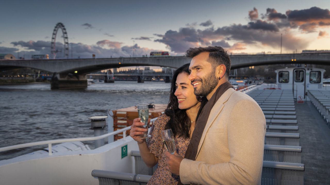 Enjoy a romantic cruise along the river this Valentine's Day. Image courtesy of Golden Tours. Two people stand on the deck of a river cruise boat drinking champagne.