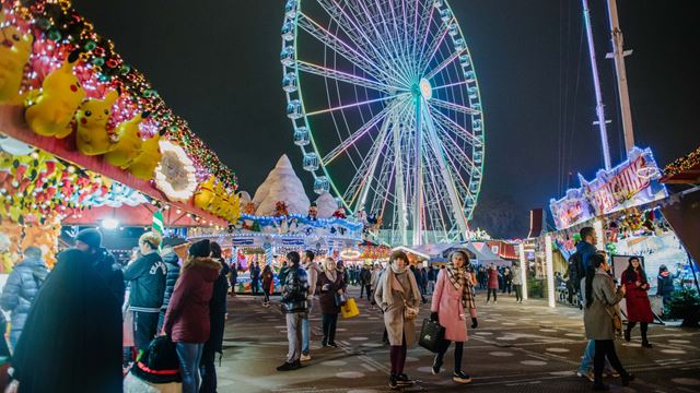 People wandering around the stalls of the Winter Wonderland with a Ferris Wheel in the background.