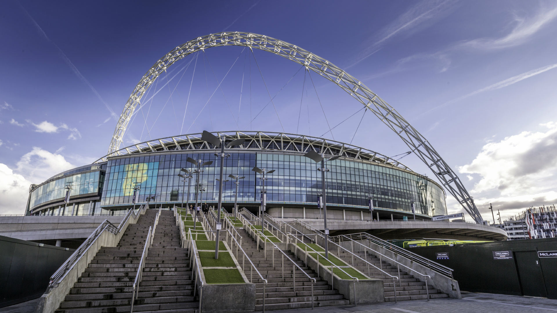 Wembley Stadium. Image credit: Visit London/Antoine Buchet. The outside of Wembley Stadium viewed from the bottom of the entrance steps with the venue's iconic arch emphasised against the blue sky.