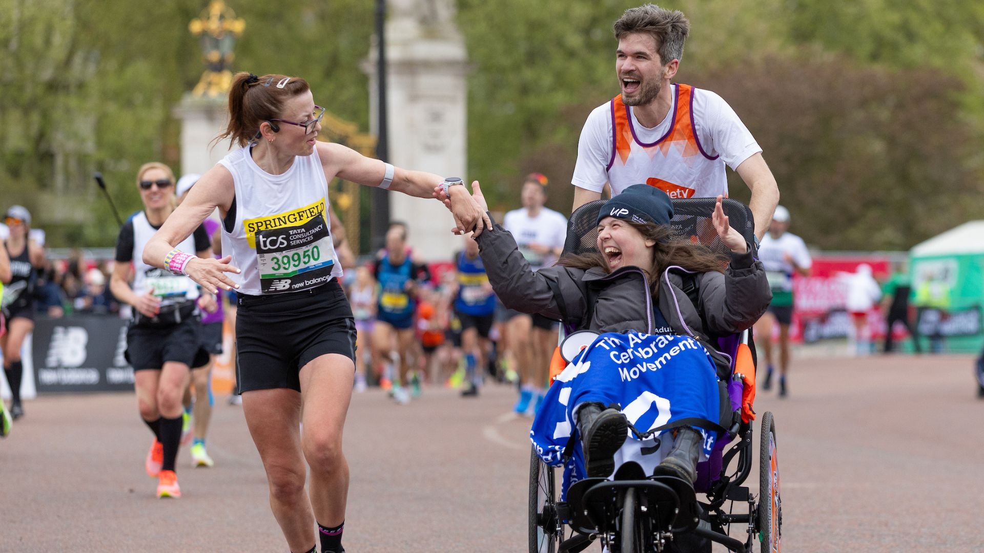 Rosie Jones and Evo Graham high five a participant a they make their way past Buckingham Palace during The TCS London Maratho. ©TCS London Marathon. Photo: Kieran Cleeves for London Marathon Events Rosie Jones and Evo Graham high five a participant a they make their way past Buckingham Palace during The TCS London Marathon on Sunday 21st April 2024.
