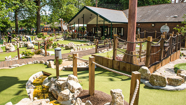 Enjoy a game of mini-golf set in a beautiful and historic London Park. Image courtesy of Putt in the Park. A mini-golf course set in a park with a clubhouse behind on a sunny day.