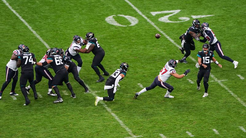 Cheer on your favourite NFL team at Wembley Stadium. Image courtesy of Jed Leicester and NFL_UK. Action shot of 12 NFL players against the bright green pitch and 20 line during Houston Texans at Jacksonville Jaguars game.