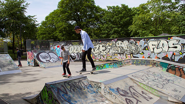 Perfect your skating tricks at Alexandra Palace Skatepark © Lloyd Winters. Image courtesy of Lloyd Winters / Alexandra Palace. Two boys on skateboards gliding over the graffitied concrete ramps at Alexandra Palace skatepark on a sunny day.