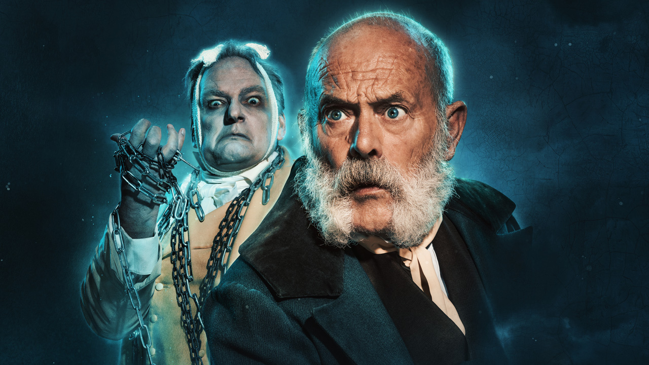 A man stands at the front wearing a black suit and looking puzzled while an eerie figure stands at the back.