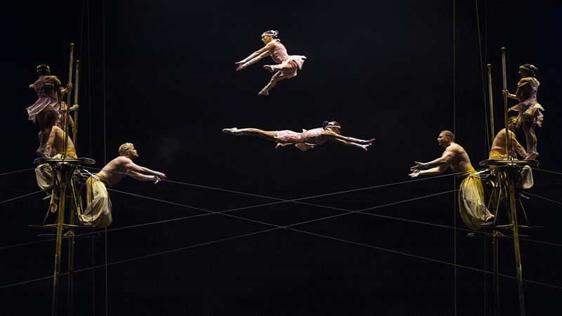 Cirque Du Doleil Corteo London. Image courtesy of London Theatre Direct, Image: Anne-Marie Forker Six acrobats are holding onto ropes and two acrobats in ballet clothing are flying in the air at between those ropes at Cirque Du Doleil Corteo London.