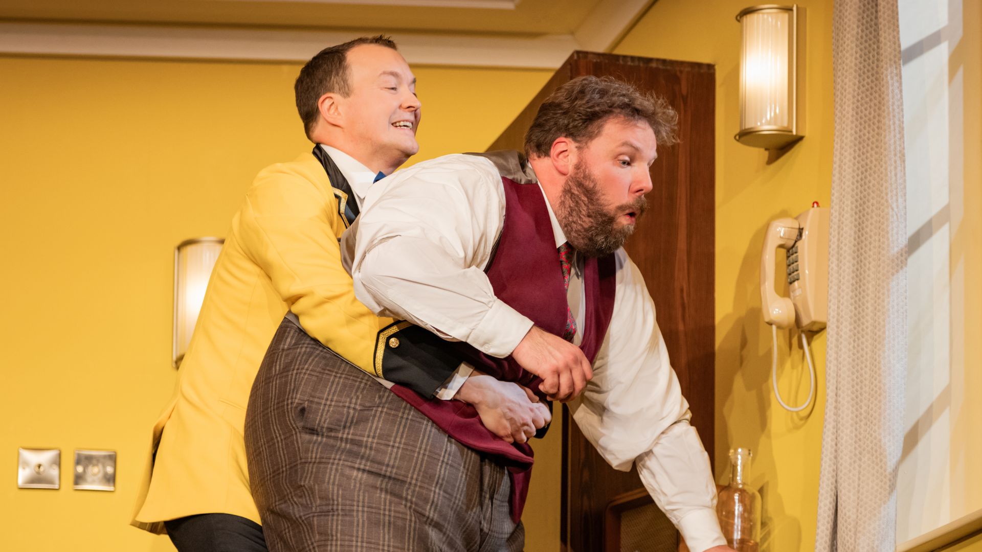 Meet hilarious hotel manager Albert Tipton and budding actor Douglas Woodbead at The Comedy About Spies. Image courtesy of London Theatre Direct. A hotel manager performs the Heimlich maneuver on a hotel guest in The Comedy About Spies
