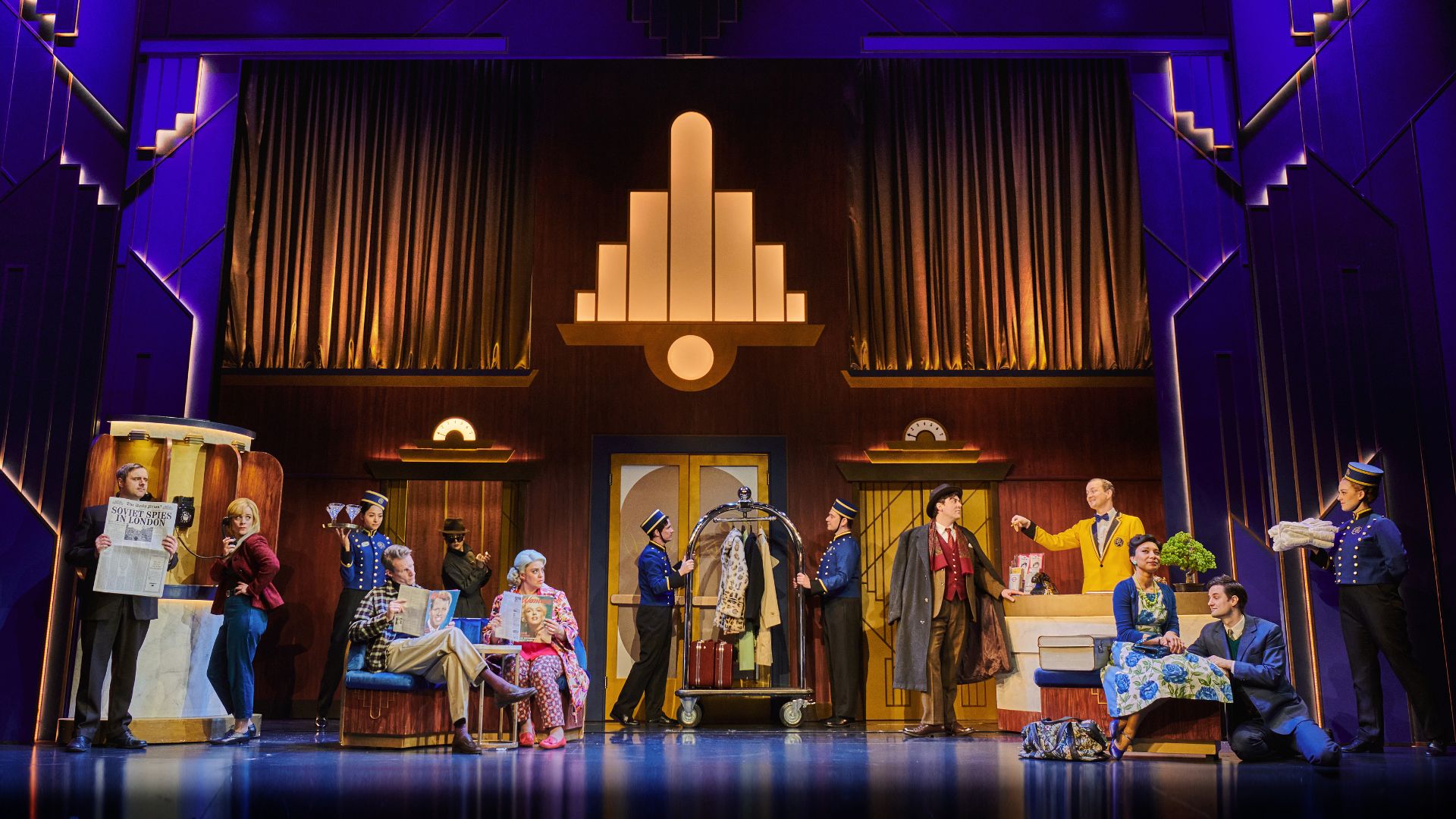 Laugh out loud at hilarious The Comedy About Spies. Image courtesy of London Theatre Direct. The cast of the comedy about spies all stand on stage in a dimly lit hotel lobby.