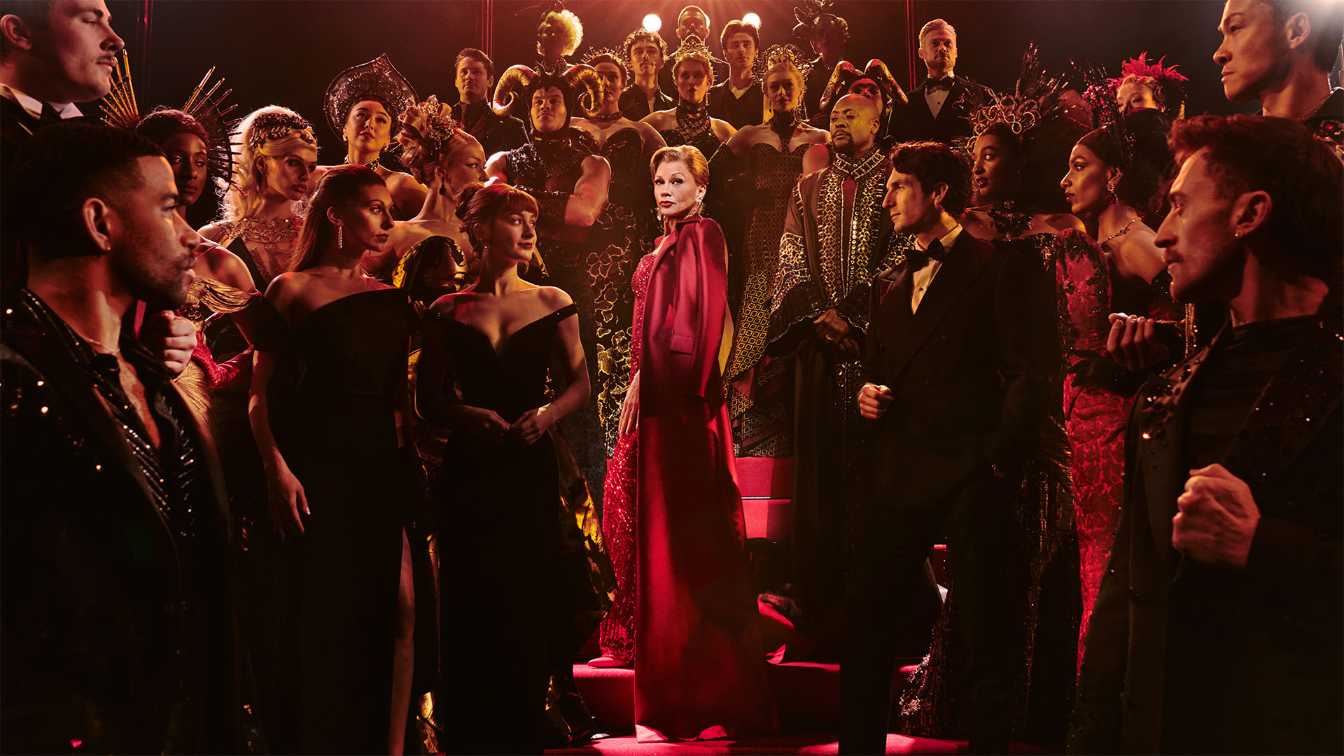 See Vanessa Williams take the spotlight as tyrant editor-in-chief Miranda Priestley in The Devil Wears Prada musical. Photo credit: London Theatre Direct. Miranda Priestly, played by Vanessa Williams, wears a glittering red dress and walks down the stairs surrounded by the cast of Devil Wears Prada.