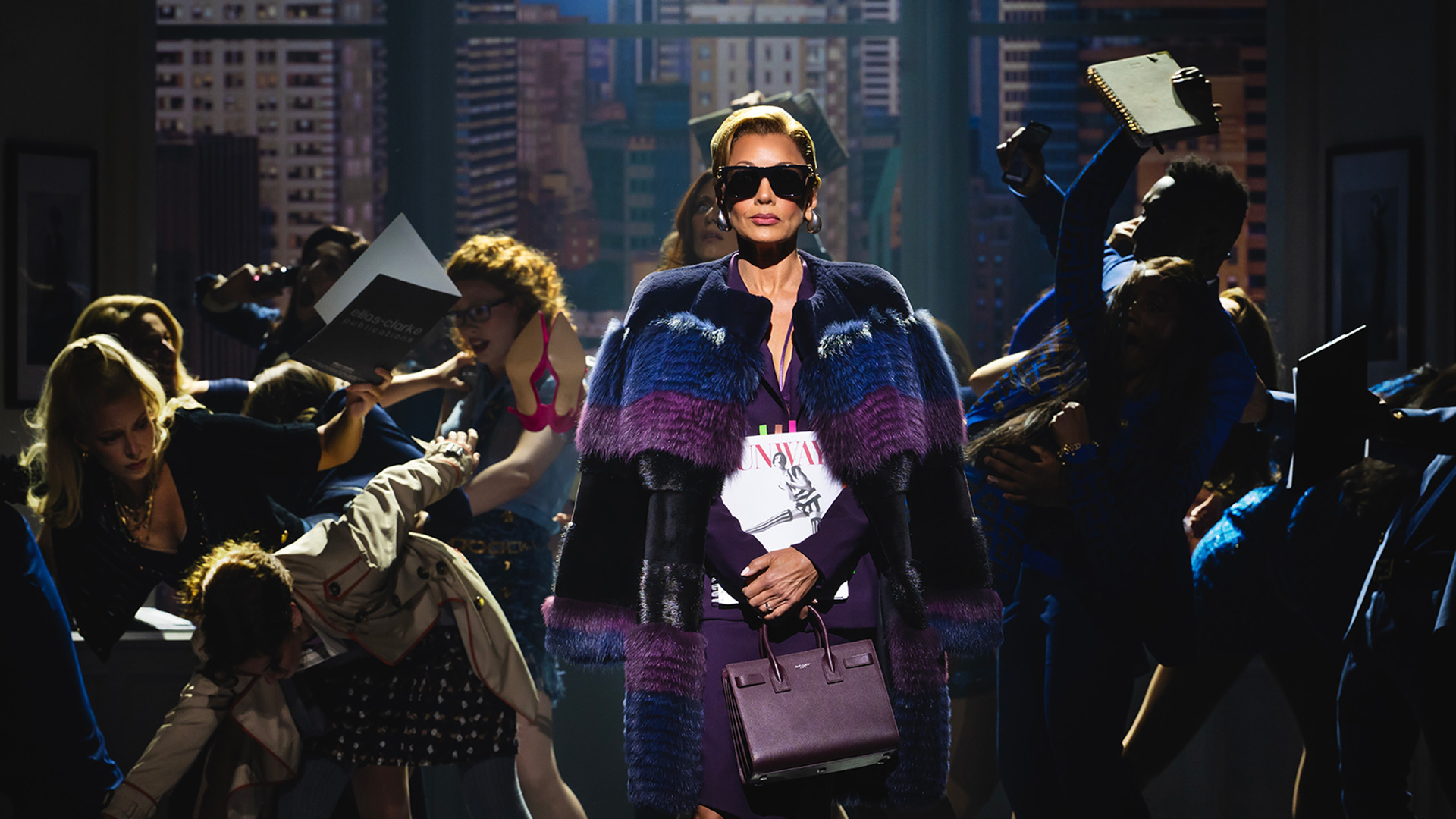 See London's latest musical sensation, as iconic film The Devil Wears Prada is brought to life on the stage at Dominion Theatre. Image courtesy of Dewynters/ Photo credit: Matt Crockett. Vanessa Williams, portraying editor-in-chief Amanda Priesley, wears black sunglasses, a purple cape and a handbag as she walks across the stage while the press ask her questions.