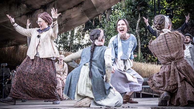 Women in conservative-looking dresses dance happily on stage during a performance of Fiddler on the Roof.