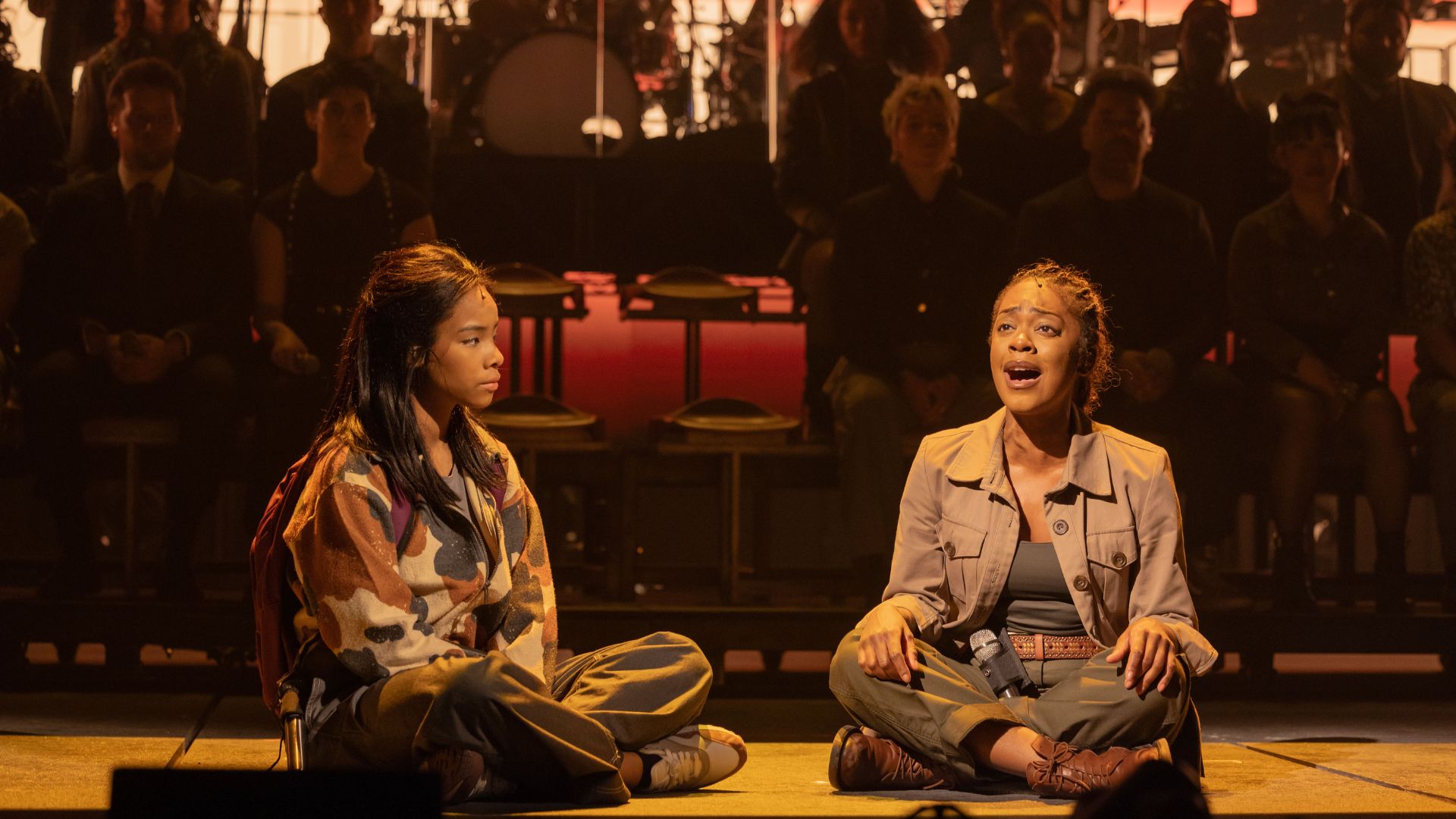 Discover the story of Live Aid, the concert that rocked the world in 1985, in the new musical Just For One Day. Image courtesy of London Theatre Direct. The cast of Just For One Day sit in the centre of the stage and perform a song, with two performers sat next to one another.