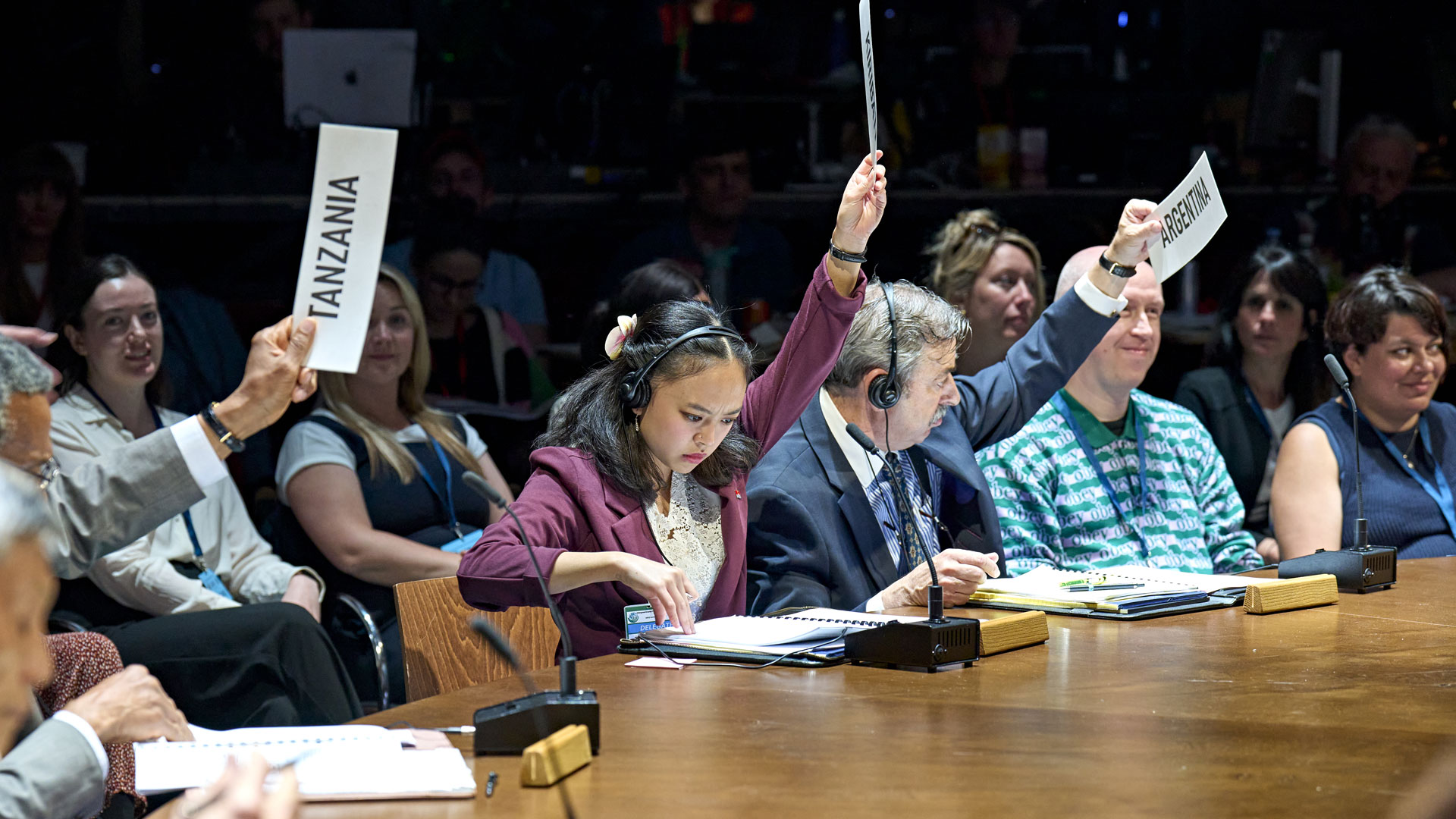 See the groundbreaking play Kyoto and immerse yourself in the first climate conference of its kind. Image courtesy of RSC and Good Chance/Photo by Manuel Harlan. The actors who play the ambassadors in the Kyoto play are holding signs with names of the countries on them.