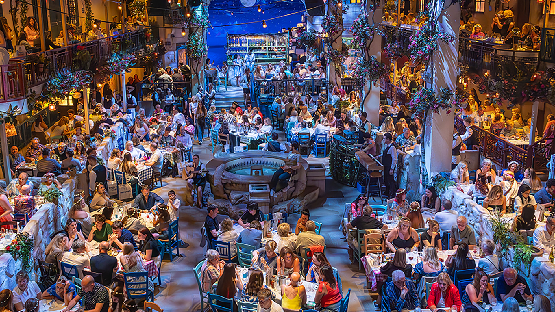Find yourself in the heart of Nikos Taverna, where family drama is paired with the best of ABBA at Mamma Mia! The Party. Image courtesy of About Grace PR. Overview of Nikos Taverna, where guests are seated at tables while the cast of Mamma Mia! Party perform the show.