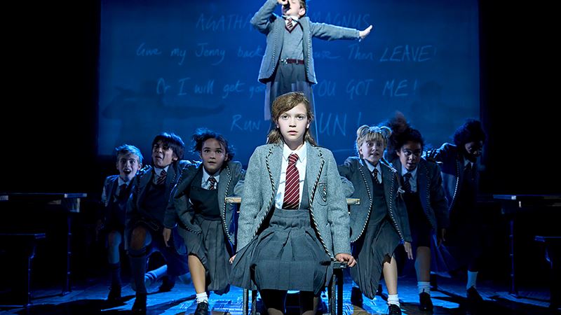 Take the kids to London and see the award-winning adaptation of Matilda The Musical and revisit Roald Dahl's famous story. Image courtesy of Storyhouse PR / Photo credit: Manuel Harlan. A girl in a school uniform sits on a chair in the centre of the stage, while other students run towards her from backstage.